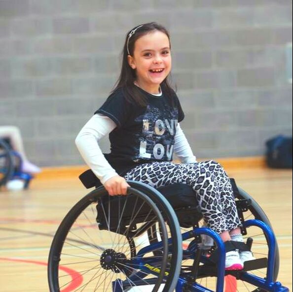 A photo of a young person using a wheelchair, and smiling.