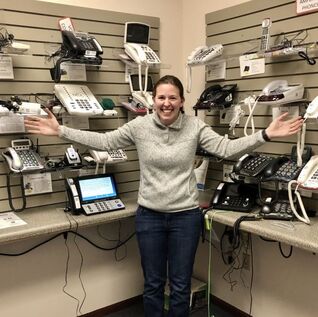 A photograph of staff member Nicole standing with arms outstretched in an assistive technology room at Access to Independence.