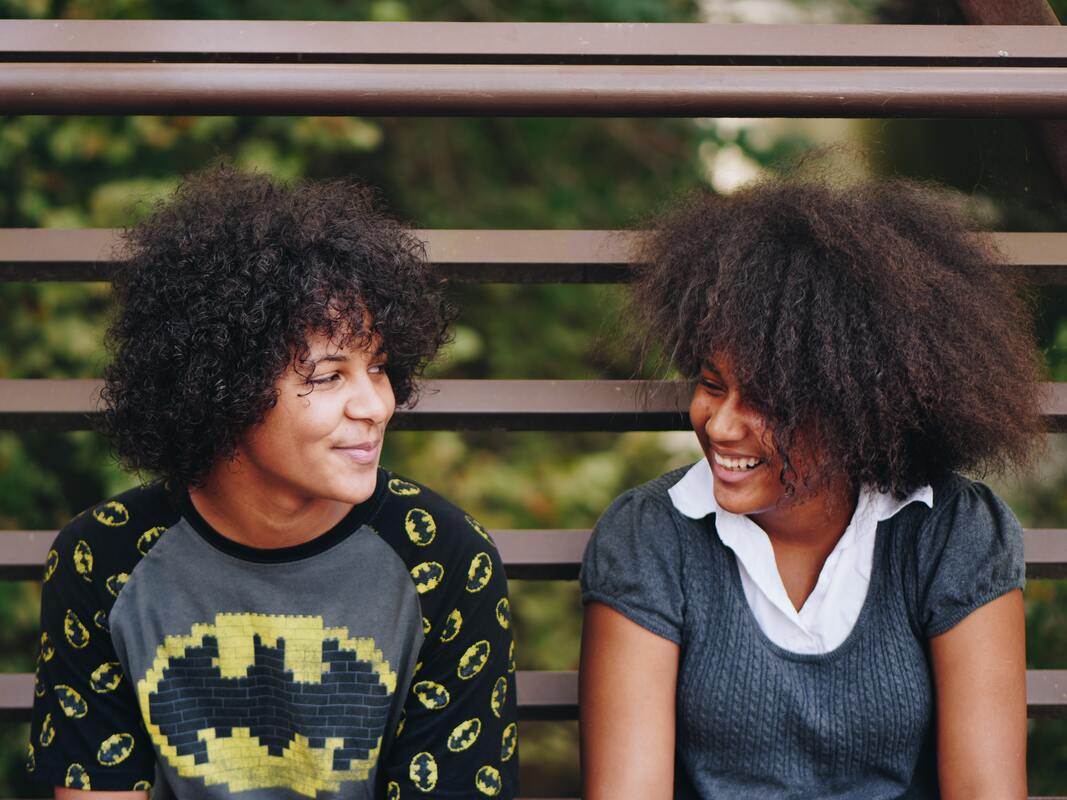A photo of two people sitting on an outdoor bench, smiling at each other.