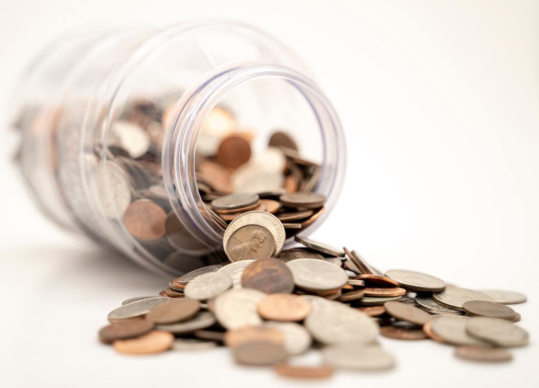 A photograph of spare change spilling out of a glass jar.