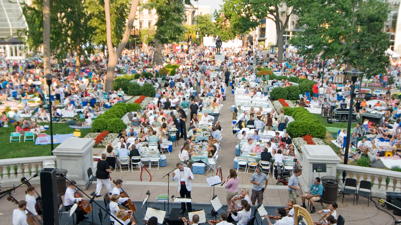 A photo of a large group of people seated outside of the Capitol building in Madison, WI watching a string ensemble