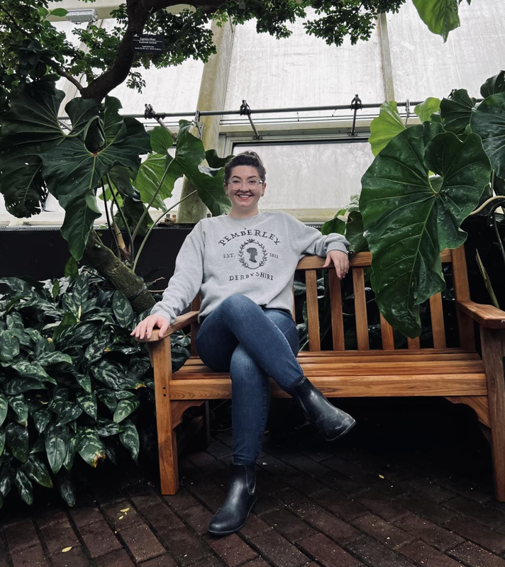 Photo of Elain sitting on a wooden bench surrounding by large, green plants